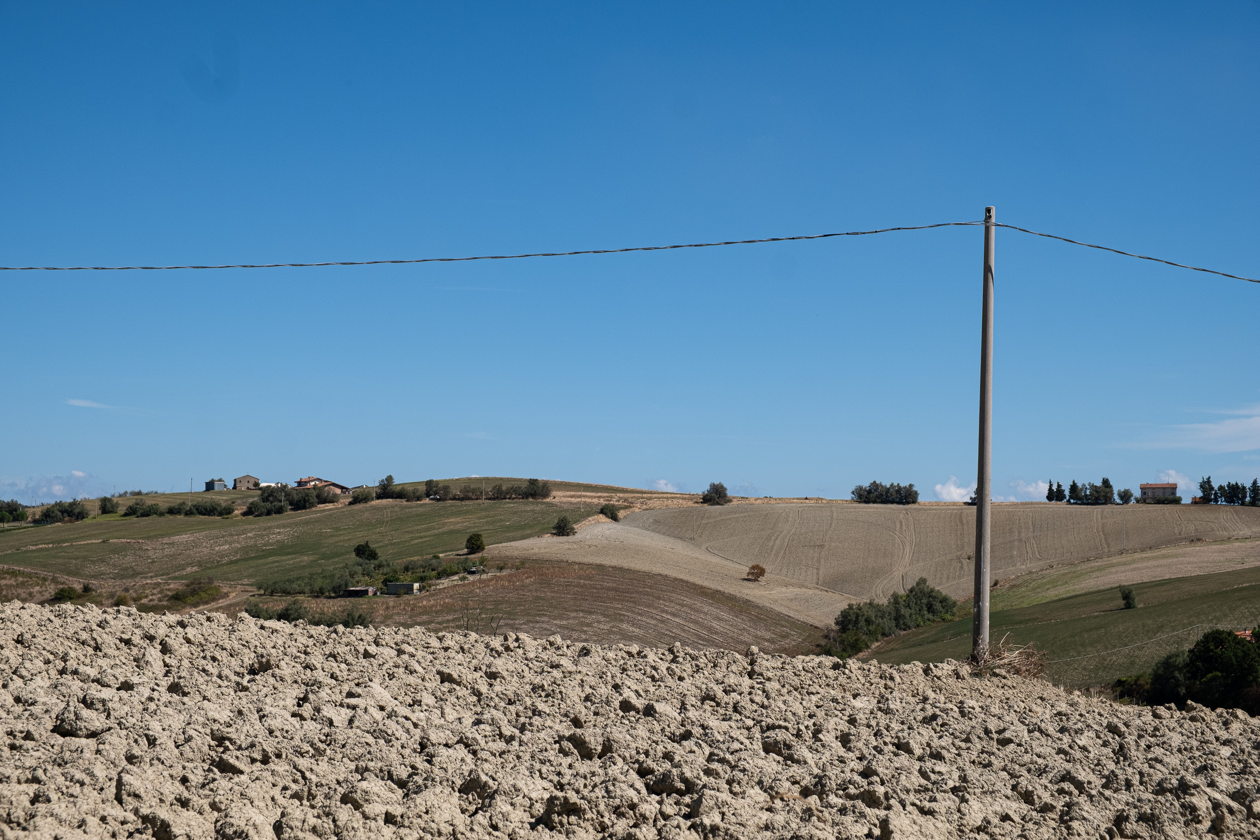 Lehmschollen und sanfte Hügel – Strommast im Feld